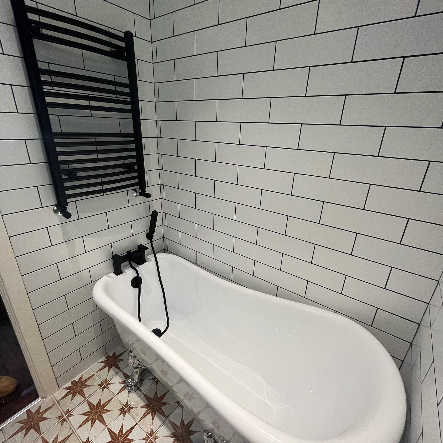 Clawfoot bath with matte-black tap and towel rail against white subway tiles