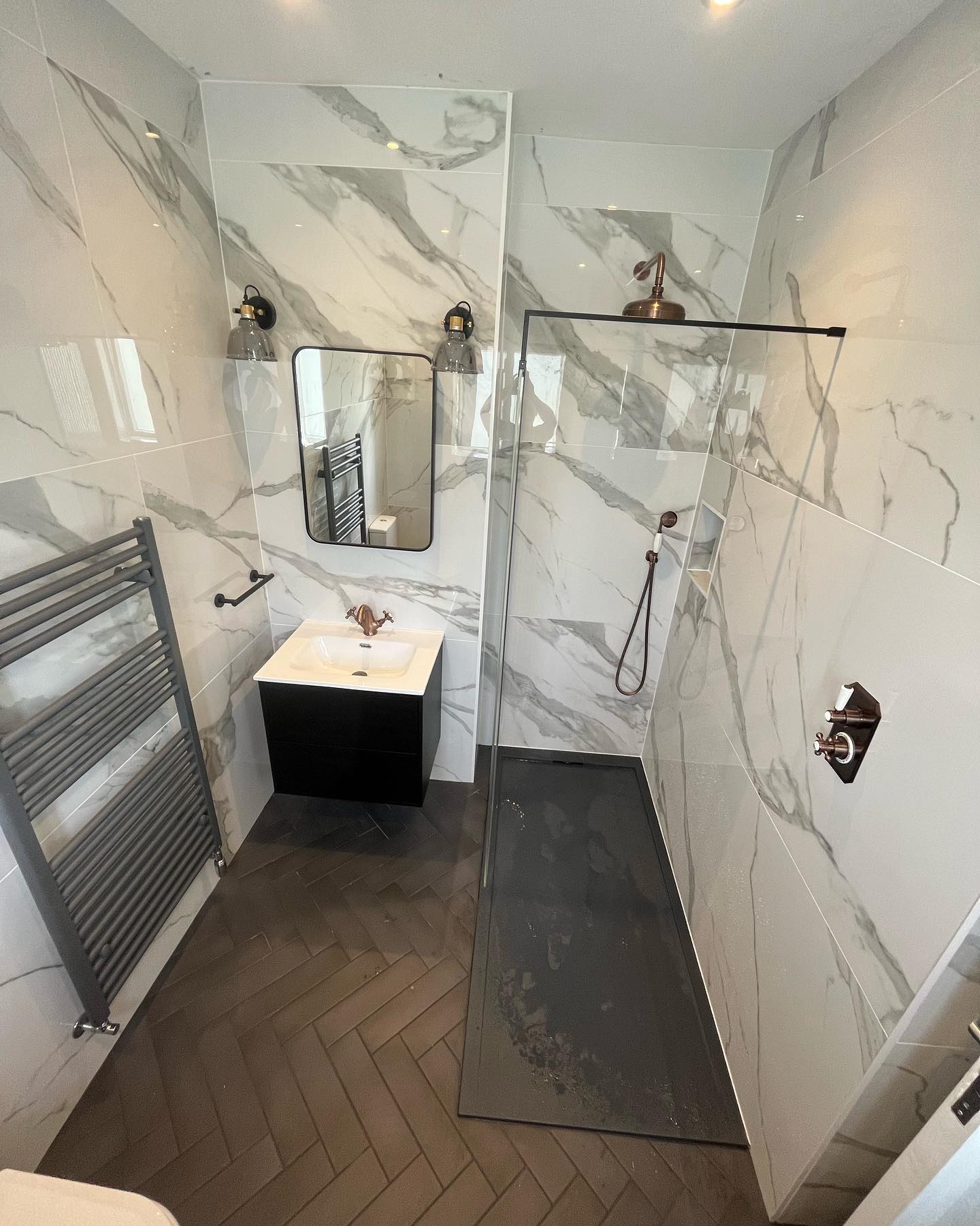 Marble-panelled bathroom with walk-in shower, herringbone floor and copper fittings