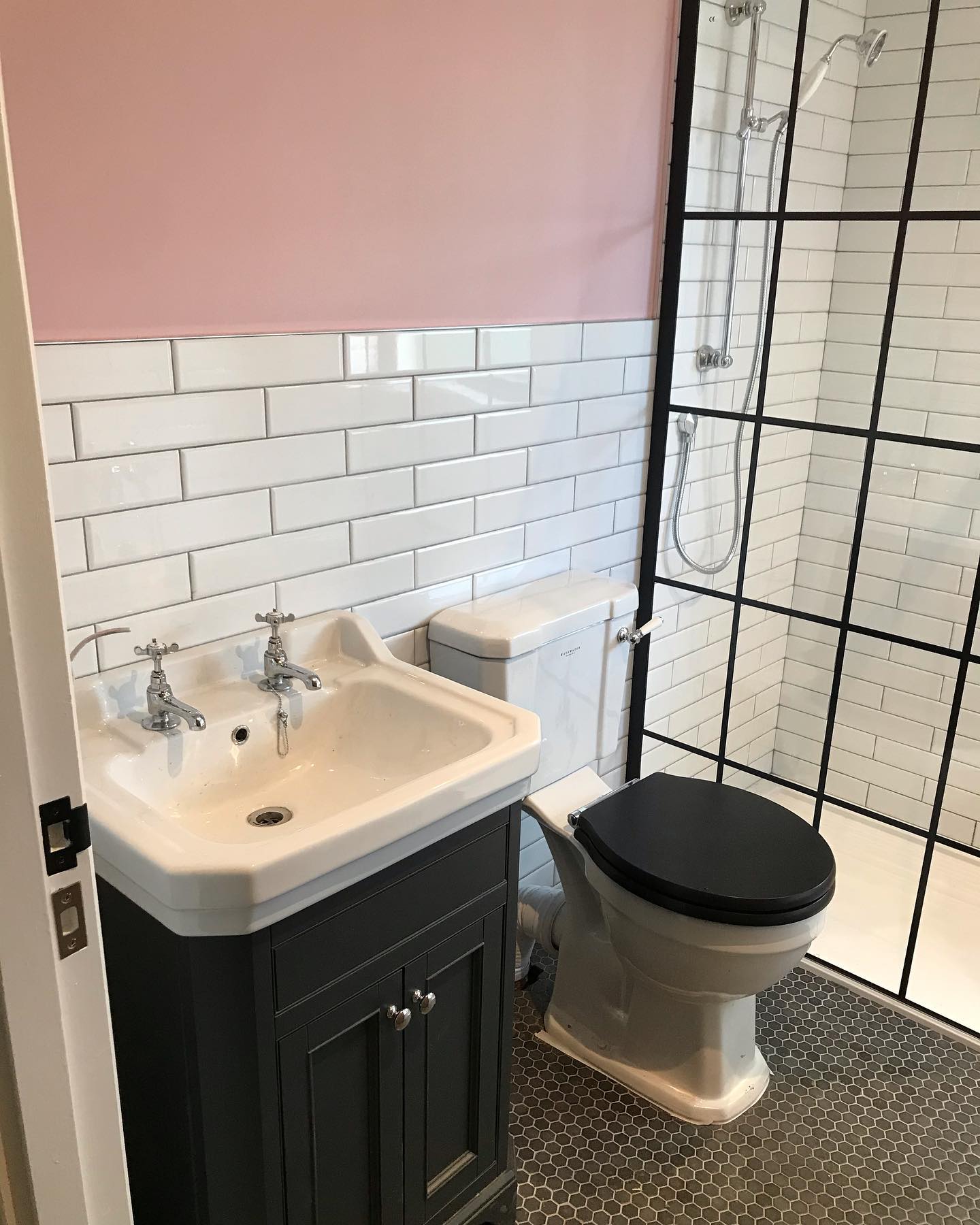 Bathroom with white subway tiles, pink upper wall, dark vanity and black-framed shower