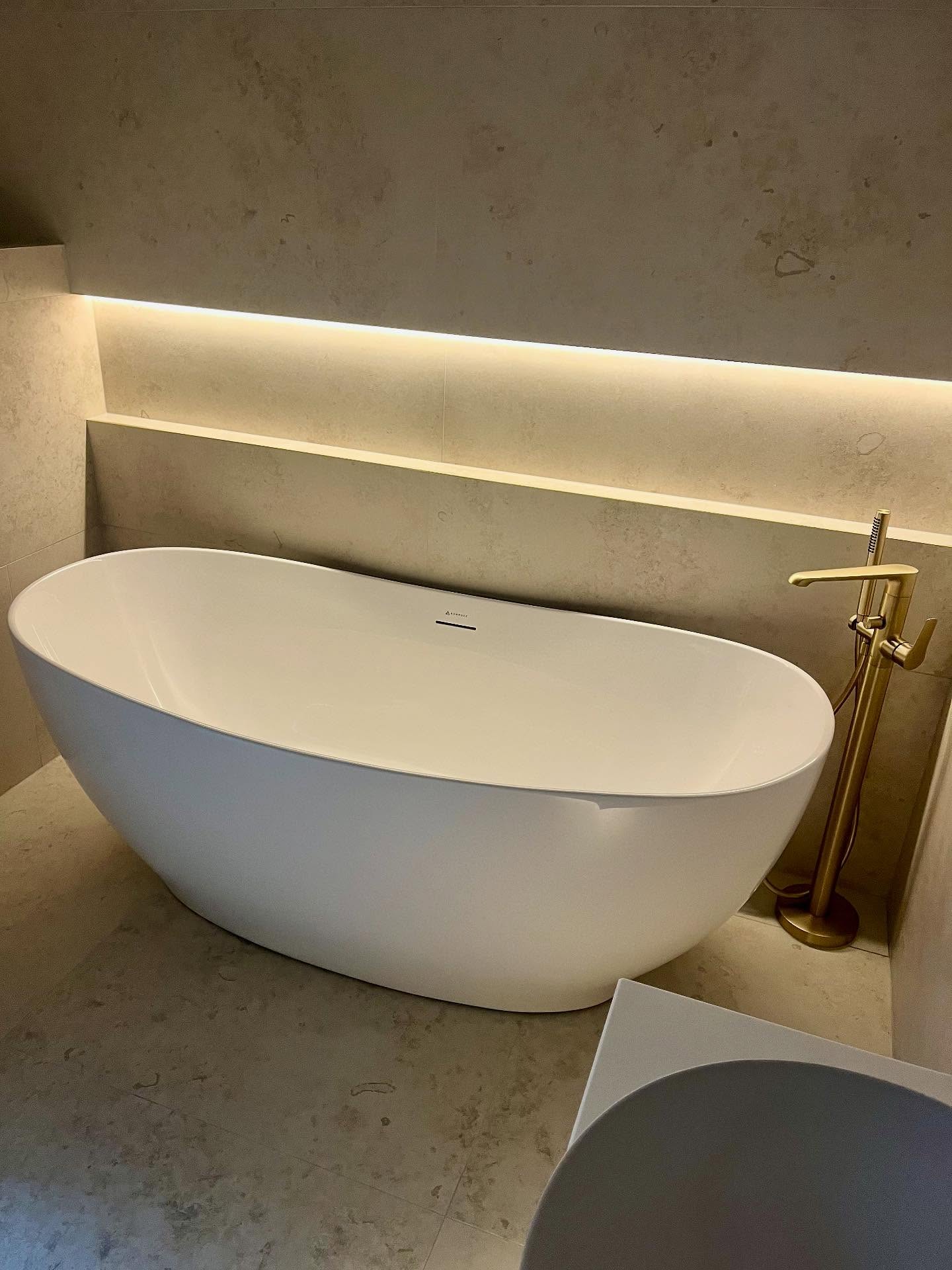 Freestanding bath with brushed brass floor-mounted tap in a stone-tiled bathroom