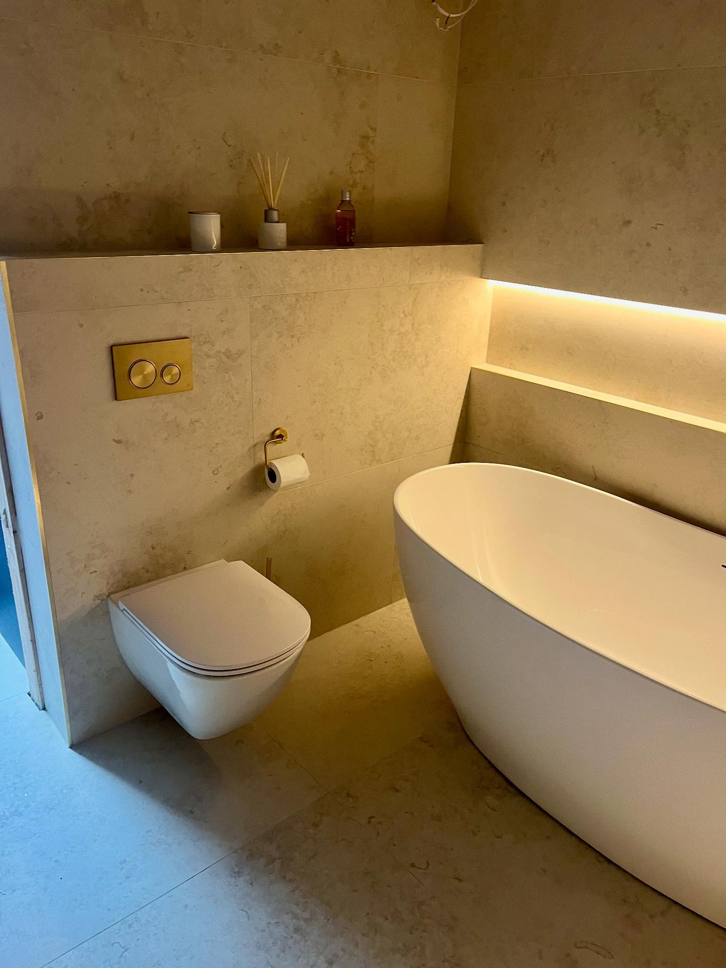 Stone-tiled bathroom with freestanding bath, wall-hung WC and warm recessed lighting