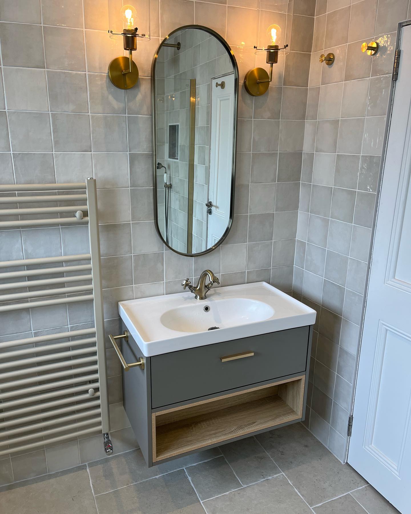 Grey square-tile wall with wall-hung vanity and brass sconces
