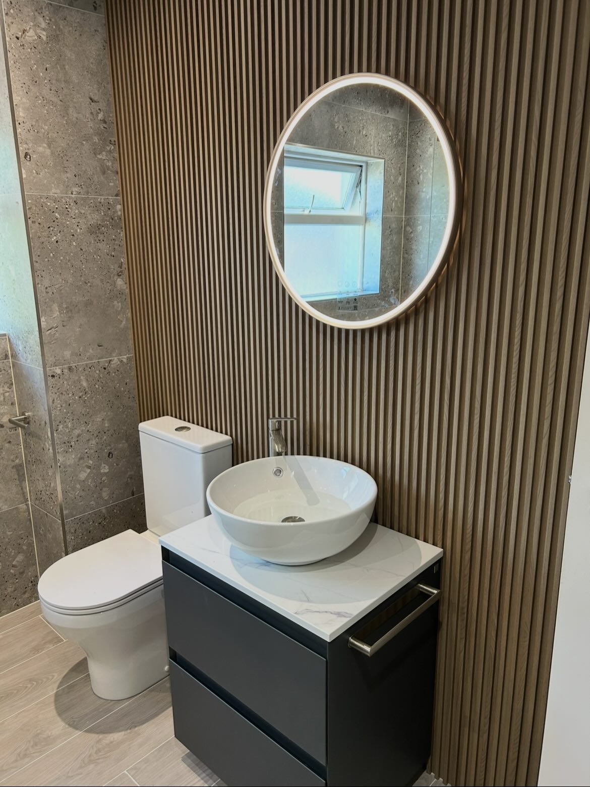 Wood-slat panelled bathroom with round LED mirror