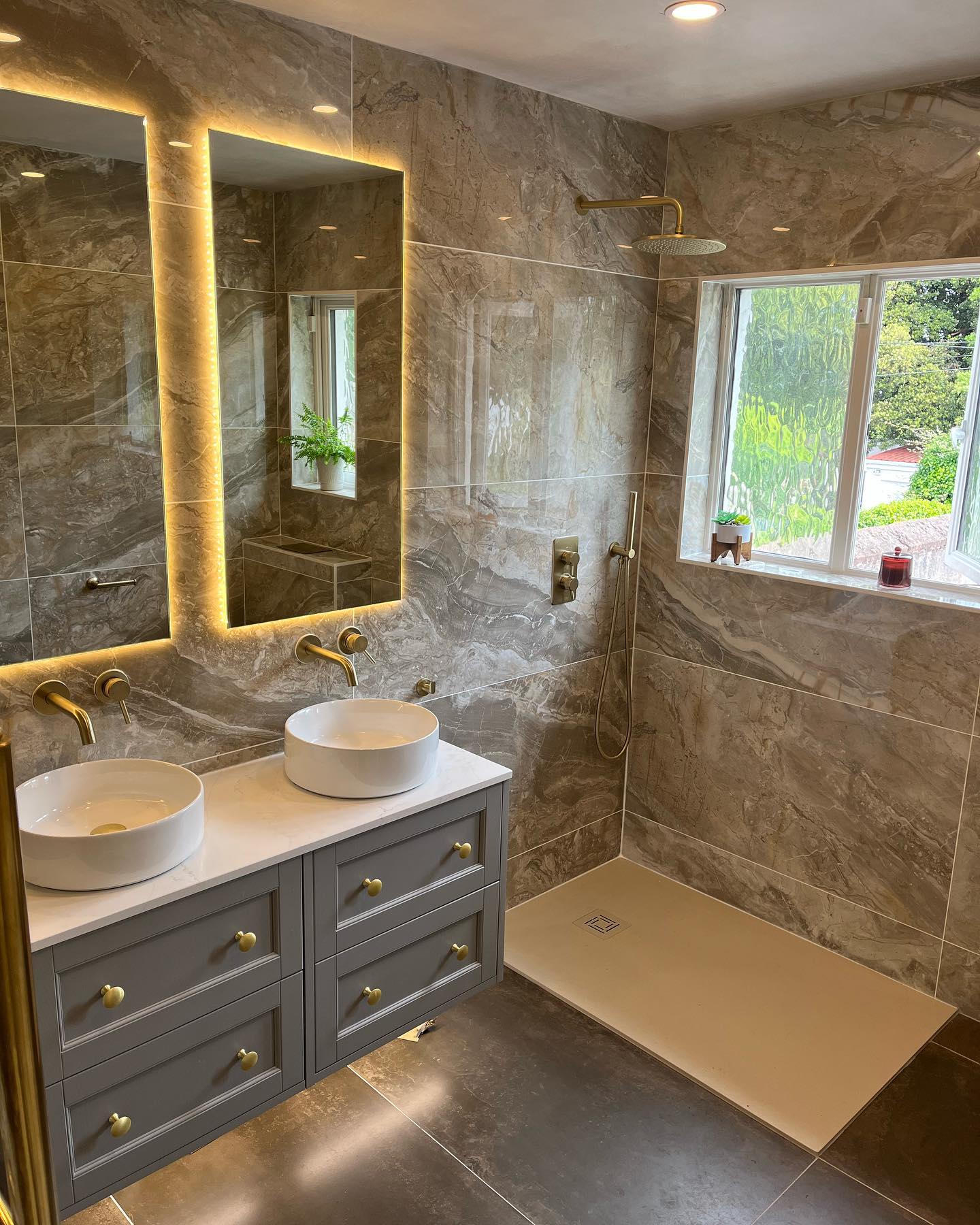 Marble-tiled bathroom with double vessel basins, brushed brass tapware and walk-in shower